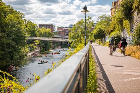 Auf dem Bild sind der Karl-Heine Kanal mit Paddelbooten und Fahrradfahrer zu sehen.